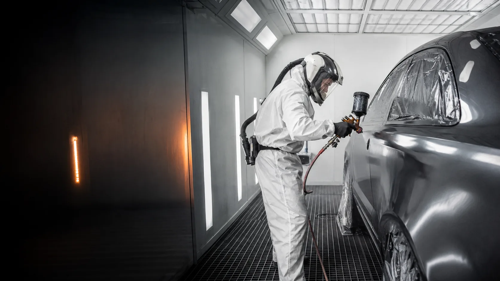 Automotive paint technician using a spray gun inside a professional spray booth